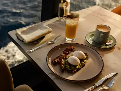 Ein appetitlich angerichtetes Frühstück mit Avocadotoast, pochierten Eiern, Speck und Kaffee am Fenster an Bord der Explora I.