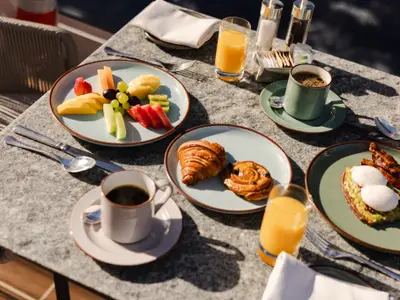 Ein gedeckter Frühstückstisch an Bord der Explora I mit frischem Obst, Gebäck, Avocado-Toast mit Ei, Kaffee und Orangensaft.