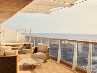 Großzügige Terrasse einer Residence-Suite an Bord der Explora I mit Whirlpool, Holzdeck, Sessel und Blick aufs Meer.