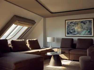 Eleganter Wohnbereich einer Suite an Bord der Explora I mit stilvollen braunen Sofas, Kunstwerk und Dachfenster.