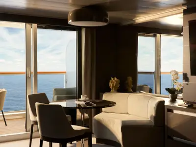 Eleganter Wohnbereich einer Suite an Bord der Explora I mit gemütlichem Sofa, Tisch und Balkon mit Meerblick.