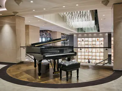 Ein schwarzer Steinway & Sons Flügel auf Parkettboden im Atrium an Bord der Explora II mit modernem Kronleuchter.