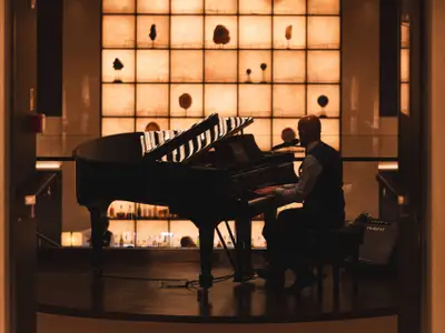 Ein Pianist im Silhouette-Profil spielt an einem schwarzen Konzertflügel in einer beleuchteten Lounge an Bord der Explora II.
