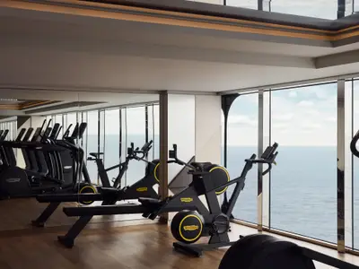 Ein modernes Fitnessstudio an Bord der Explora II mit Technogym-Geräten und großen Fenstern zum Meer.
