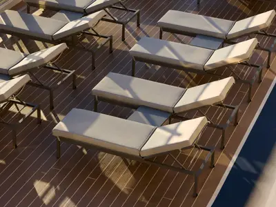 Elegante Sonnenliegen mit grauen Polstern auf einem Holzdeck an Bord der Explora II im Tageslicht.