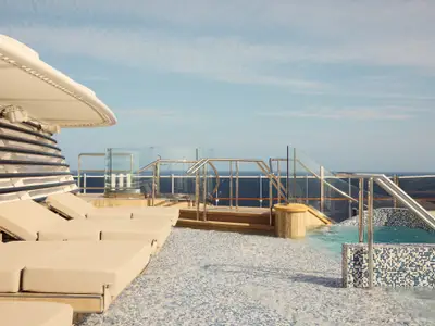 Sonnendeck an Bord der Explora II mit beigen Sonnenliegen, kleinem Pool mit blauen Mosaikfliesen und Blick auf das Meer.