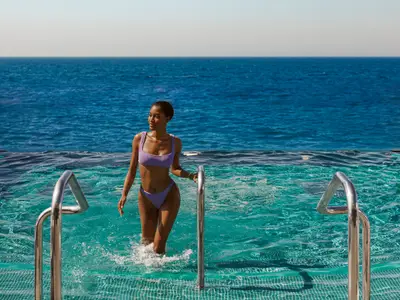 Eine Frau im violetten Bikini steigt im Infinity-Pool an Bord der Explora II aus dem Wasser mit Blick aufs offene Meer.