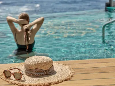 Eine Frau entspannt im Pool an Bord der Explora II. Im Vordergrund liegen ein Strohhut und eine Sonnenbrille auf dem Holzdeck.