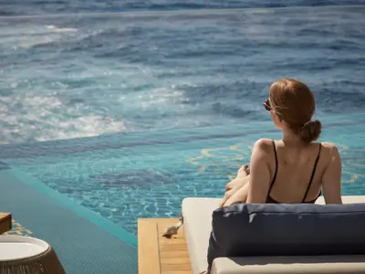 Eine Frau im Badeanzug sitzt auf einer Liege am Infinity-Pool an Bord der Explora II und blickt aufs blaue Meer.