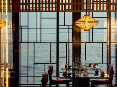 Eindeckter Tisch in einem eleganten Restaurant an Bord der Explora II mit direktem Blick durch Gitterfenster auf das Meer.