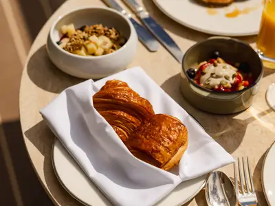 Ein Tisch mit frisch gebackenen Croissants in einer Stoffserviette und Müslischalen an Bord der Explora II.