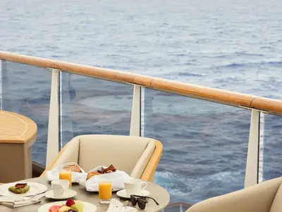 Gedeckter Frühstückstisch mit Orangensaft und Gebäck auf dem Balkon an Bord der Explora II vor blauem Meer.