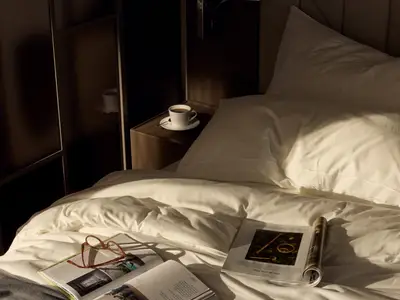 Warmes Sonnenlicht fällt auf das weiße Bett, ein Buch und eine Kaffeetasse in einer Suite an Bord der Explora II.