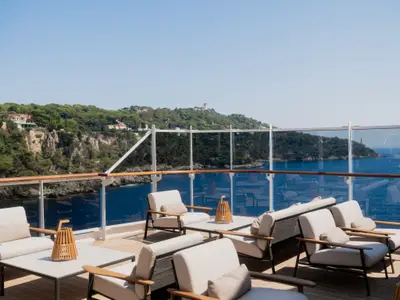 Außenbereich der Sky Bar an Bord der Explora III mit bequemen Loungesesseln, Holzakzenten und Panoramablick auf die Küste.