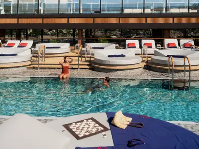Ein Mann schwimmt im Pool, während eine Frau am Beckenrand an Bord der Explora III entspannt. Dahinter befinden sich Sonnenliegen.