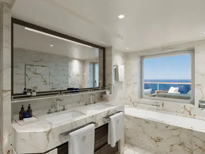 Elegantes Badezimmer aus hellem Marmor mit Doppelwaschbecken, Badewanne und Fensteraussicht aufs Meer an Bord der Explora III.