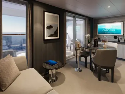 Elegante Suite an Bord der Explora III mit Esstisch, Champagner, Fernseher und Meerblick durch den Balkon.