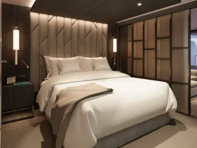 Luxuriöses Doppelbett mit weißer Bettwäsche, kunstvoller Kopfteilwand und warmem Licht an Bord der Explora III.