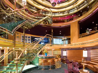 Blick auf das elegante Atrium an Bord der Eurodam mit einer gläsernen Treppe, einer Bar und komfortablen Sitzbereichen.