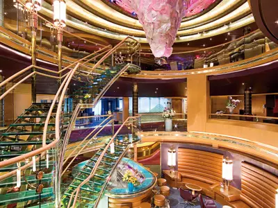 Blick auf das dreistöckige, luxuriös gestaltete Atrium an Bord der Eurodam mit einer geschwungenen Glastreppe.
