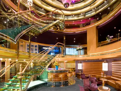 Blick auf das prachtvolle Atrium an Bord der Eurodam mit geschwungenen Glastreppen, goldener Architektur und einer gemütlichen Bar.