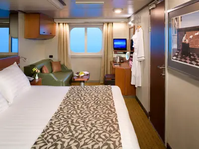 Eine geräumige Außenkabine mit Doppelbett, grünem Sofa und Meerblick durch das Fenster an Bord der Eurodam.
