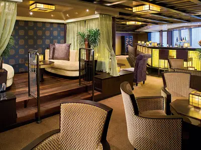 Elegante Sessel und eine beleuchtete Bar in der asiatisch inspirierten Silk Den Lounge an Bord der Eurodam.