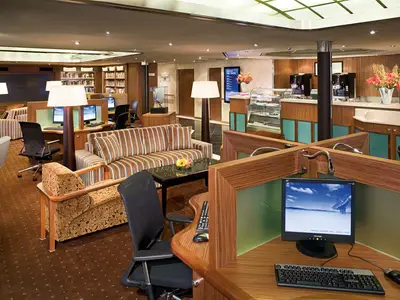 Blick in das Explorations Café an Bord der Eurodam mit Arbeitsplätzen für Computer, Sesseln, Sofas und Bücherregalen.