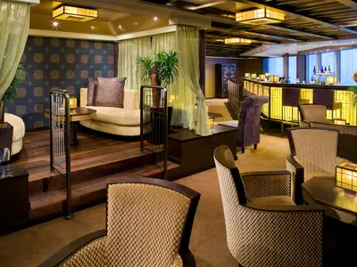 Blick in die asiatisch inspirierte Silk Den Lounge an Bord der Eurodam mit gemütlichen Sitzbereichen und einer beleuchteten Bar.
