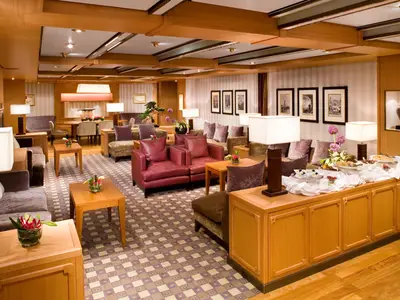 Die stilvoll eingerichtete Neptune Lounge an Bord der Eurodam mit roten Ledersesseln, Holzmöbeln und Buffet.