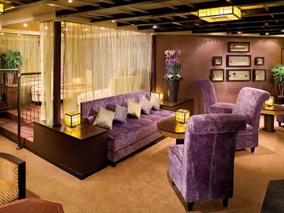 Blick in die gemütlich beleuchtete Silk Den Lounge an Bord der Eurodam mit lila Polstermöbeln und asiatischem Dekor.