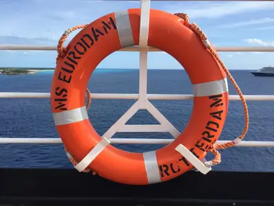 Orangefarbener Rettungsring mit der Aufschrift MS Eurodam Rotterdam an einer weißen Schiffsreling vor blauem Meer und Himmel.