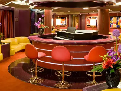 Blick auf die kreisrunde rote Piano Bar mit Barhockern und einem Flügel im Zentrum an Bord der Eurodam.