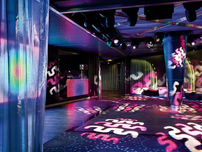 Der farbenfrohe Nachtclub Northern Lights an Bord der Eurodam zeigt eine beleuchtete Tanzfläche mit Wellenmustern, Vorhängen und gemütlichen Sitzecken.