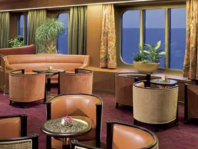 Eine gemütliche Lounge an Bord der Eurodam mit bequemen Sesseln, runden Tischen und großen Fenstern mit Blick auf das blaue Meer.