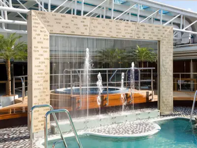Ein kunstvolles Wasserspiel mit eingravierten Woertern vor einem Whirlpool am Pooldeck an Bord der Eurodam.