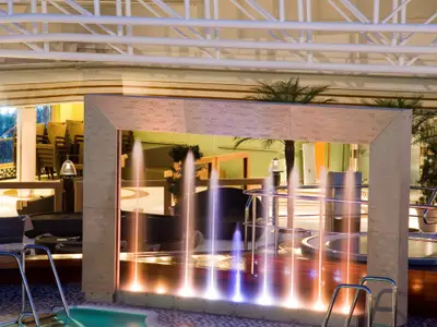 Eine beleuchtete Steinskulptur mit Wasserfontänen am abendlichen Lido-Pool an Bord der Eurodam.