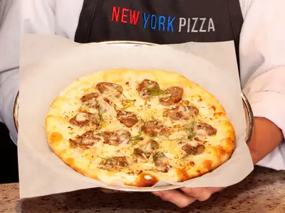 Eine frisch gebackene Pizza mit Wurst und Käse, präsentiert von einem Koch an Bord der Eurodam.