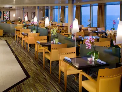 Gedeckte Tische und gelbe Sessel im hellen Lido Restaurant an Bord der Eurodam mit Blick auf das weite Meer.