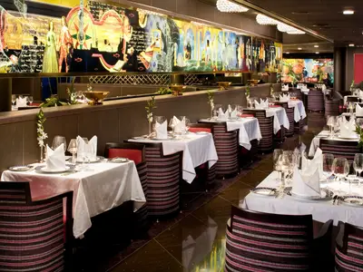 Festlich gedeckte Tische im Restaurant Pinnacle Grill an Bord der Eurodam mit kunstvollem Wandbild im Hintergrund.
