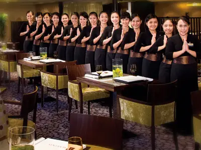 Eine Reihe lächelnder Servicemitarbeiterinnen in schwarzer Kleidung begrüßt die Gäste im Tamarind Restaurant an Bord der Eurodam.