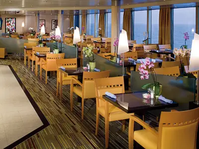 Speisebereich an Bord der Eurodam mit eleganten Holzmöbeln und großen Fenstern, die einen weiten Blick auf das offene Meer bieten.