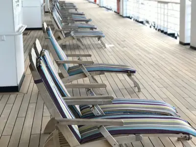 Reihe von traditionellen Holzliegestühlen mit gestreiften Auflagen auf dem Außendeck an Bord der Eurodam.