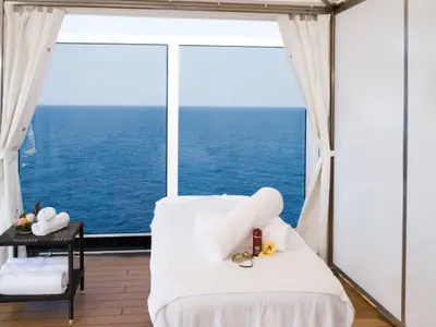 Massagebereich an Bord der Eurodam mit einer Massageliege, weißen Handtüchern und Blick durch ein Panoramafenster auf das weite Meer.