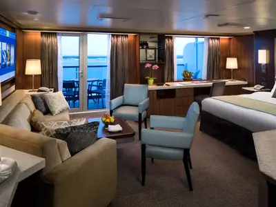 Blick in eine geräumige, elegante Suite an Bord der Eurodam mit Sitzecke, großem Bett und Balkon mit Meerblick.