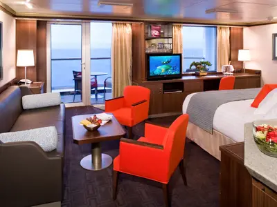 Eine luxuriöse Suite an Bord der Eurodam mit braunem Sofa, roten Sesseln, Doppelbett und Zugang zum Balkon.