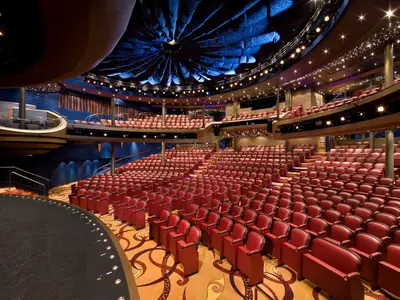 Ein weitwinkliger Blick auf die roten Samtsitze und die Bühne im eleganten Theatersaal Mainstage an Bord der Eurodam.