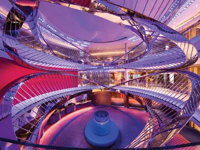 Blick in das spektakuläre Atrium an Bord der Koningsdam mit einer futuristischen, geschwungenen Metallskulptur und farbigen Lichtinstallationen.