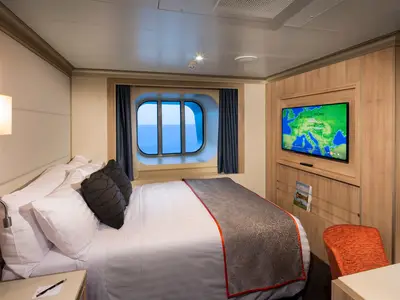 Eine gemütliche Außenkabine an Bord der Koningsdam mit einem Doppelbett, großem Fenster mit Meerblick und einem Fernseher an der Wand.