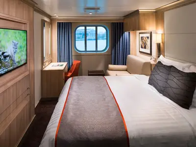 Eine helle Außenkabine an Bord der Koningsdam mit großem Doppelbett, Sitzecke, Schreibtisch und Fenster.